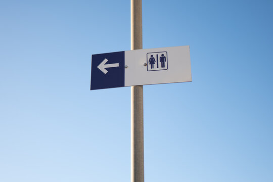 Restroom direction sign against clear blue sky