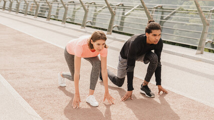 Naklejka premium Young mixed-race couple friends athletes running jogging together in fitness outfit on city urban bridge. Burning calories workout exercises outdoors.
