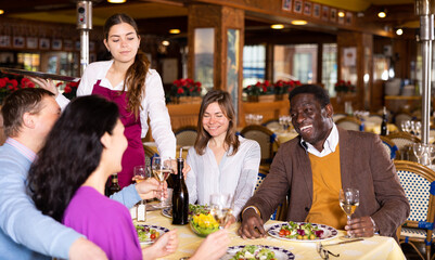 Group of joyous friends enjoying evening meal at cozy restaurant