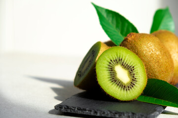 Ripe kiwi fruits in sunlight. Heap of whole kiwi fruits with green leaves and fresh cut kiwi on...
