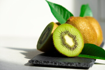 Ripe kiwi fruits in sunlight. Heap of whole kiwi fruits with green leaves and fresh cut kiwi on...