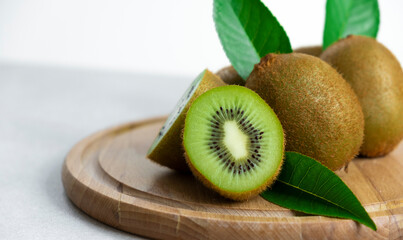 Ripe kiwi fruits in sunlight. Heap of whole kiwi fruits with green leaves and fresh cut kiwi on...