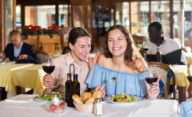 Two positive females dining in restaurant, enjoying meal and conversation