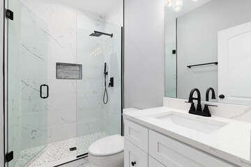 A bathroom with a white cabinet and marble countertop, black faucet and showerhead, and a marble...