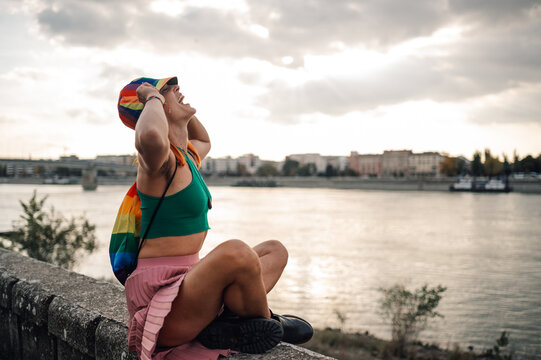 Young non binary person wearing rainbow clothes enjoying the sunset over river