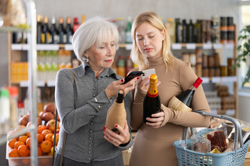 Elderly mother and her adult daughter scan a QR code on a bottle of wine label together to check the expiration date