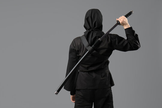 Male ninja with sword on grey background, back view