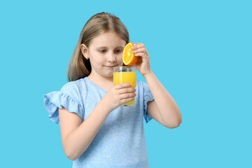 Cute little girl with glass of juice and orange on blue background