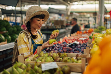 Asian woman examining pears at colorful market produce stand