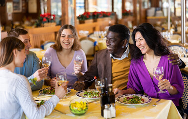 Group of adult men and women having friendly meeting at dinner in restaurant, carefree talking and drinking wine ..