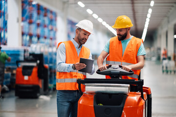 Warehouse workers driving forklift and using tablet in large distribution center