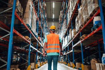 Warehouse worker walking through large warehouse with high shelves full of goods
