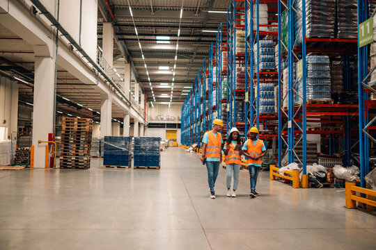 Warehouse workers walking and discussing logistics with digital tablet