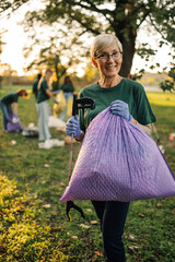 Senior volunteer collecting trash in park with other volunteers