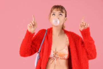 Stylish young woman with chewing gum pointing at something on pink background