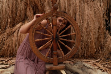 Portrait of a young beautiful woman with a spinning wheel against the background of hay