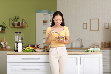 Beautiful young happy Asian woman with bowl of fresh vegetable salad in kitchen