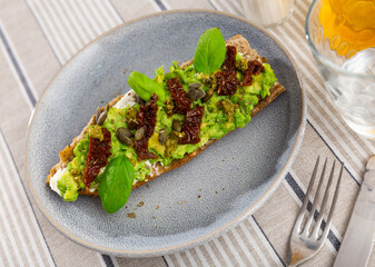 Appetizing sandwich with cheese and guacamole, dried tomatoes and seeds served on plate