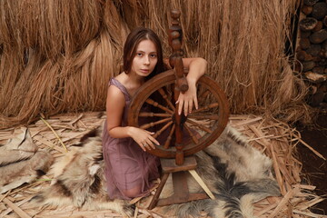 Portrait of a young beautiful woman with a spinning wheel against the background of hay