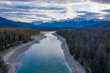 Aerial view of a Athabasca River winding through a mountain valley. Snowy peaks in the distance....