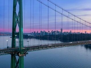Aerial view of the Lions Gate Bridge at sunset. Cars travel across the bridge, with the city skyline in the background.  Vancouver, British Columbia, Canada