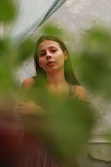 Art portrait of young brunette woman through green plants