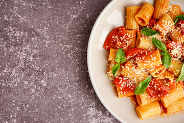 Plate of delicious penne pasta with tomato and basil on grunge background
