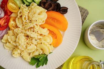 Plate with delicious Italian pasta salad on green background