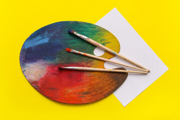 Artist brushes, palette and sheet of paper on yellow background