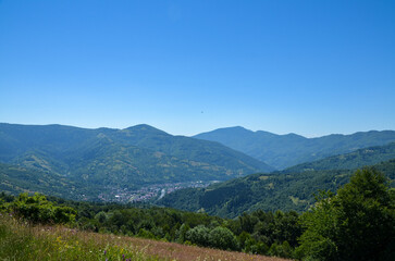 Naklejka premium Breathtaking view of a mountain valley showcasing a picturesque Rakhiv town, lush green vegetation, and surrounding hills under a clear blue sky. Carpathian Mountains, Ukraine