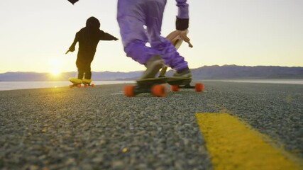 Low, slow motion shot of long boarders in silly costumes riding down desert road at sunset