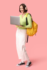 Fototapeta premium Beautiful young woman in headphones working with modern laptop on pink background