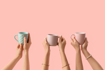 Female hands with different mugs on pink background