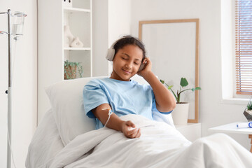 Teenage African-American girl with headphones and infusion drip in hospital room