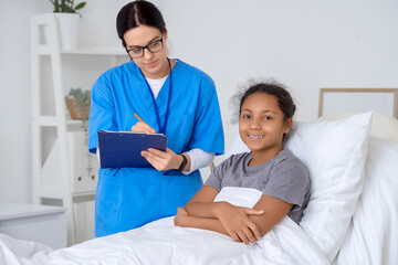 Fototapeta premium Female doctor working with teenage African-American girl in hospital room