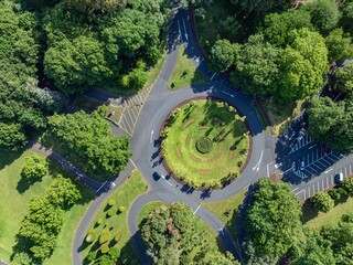 High-angle view of a park roundabout with traffic and parking. Well-maintained landscaping and...