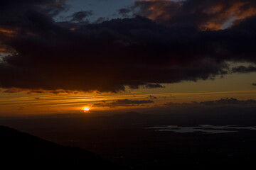 Sun hiding on the horizon with reddish and orange tones at sunset horizontally