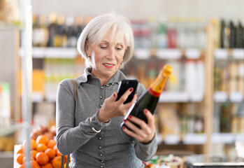 Elderly woman buyer scanning qr code for bottle of champagne in grocery store