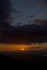 Sun hiding on the horizon with reddish and orange tones at sunset vertically
