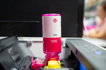 Closeup Refilling ink into a red ink tank printer at office. Cartridges and containers of...