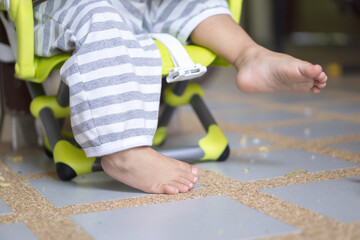 Young child's bare feet dangling from a high chair with messy food leftovers on the floor.