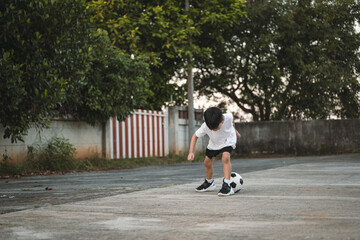 A 6 years old Asian boy kicking the ball as playing outdoor.