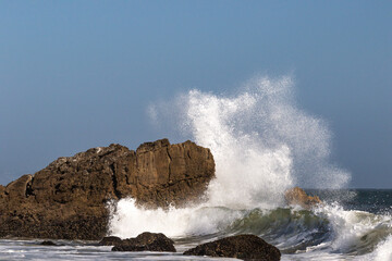 Wave breaking on rock near the shore in Malibu, California. Pacific Ocean in the background. 
