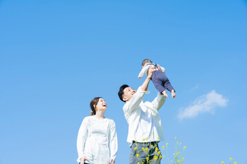 青空のもと、赤ちゃんを高く抱き上げる父母