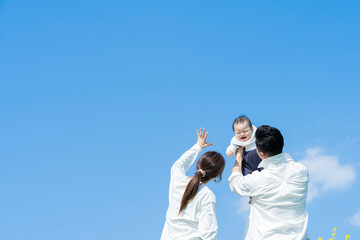 青空のもと、赤ちゃんを高く抱き上げる父母