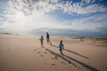 Two children chasing father on sand dune