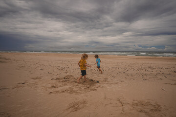 Two brothers running on beach with storm in background