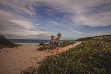 Two matching children walking on sand dune in front of sea