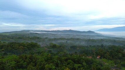 Dramatic Aerial drone view of countryside and hills with lush green trees with morning mist above with mountain range as background