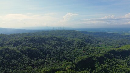 Dramatic Aerial drone view of hills with lush green trees with morning mist above with a background of rows of mountains